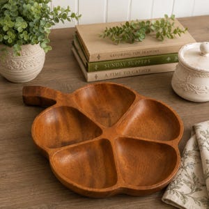 May include: A brown wooden serving tray shaped like a pumpkin with five distinct compartments and a small handle. The tray features a smooth, polished finish with visible wood grain patterns, providing a functional and segmented surface for food.