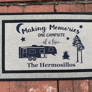 May include: A gray doormat with black trim and text that reads "Making Memories One Campsite at a time" with a silhouette of a camper, a campfire, and two pine trees. The text "The Hermosillos" is at the bottom of the mat.