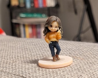 May include: A small figurine of a person with long brown hair, wearing an orange long-sleeved sweater, dark blue jeans, and brown boots. The figure is standing on a circular base, winking with one eye and holding up a peace sign with one hand.