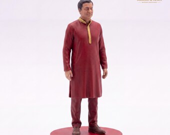 May include: A miniature figurine of a person standing on a circular red base. The figure wears a long-sleeved, knee-length dark red tunic with a gold-colored collar detail and matching dark red trousers, paired with brown shoes.