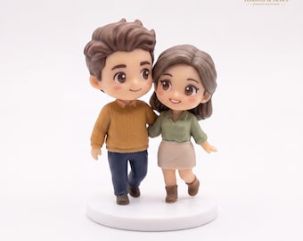 Könnte beinhalten: Eine Miniaturfigur von zwei Personen, die nebeneinander auf einem runden weißen Sockel stehen. Die linke Figur hat braunes Haar, einen senfgelben Pullover und eine dunkelblaue Hose. Die rechte Figur hat braunes Haar, ein salbeigrünes Hemd, einen beigen Rock und braune Stiefel.