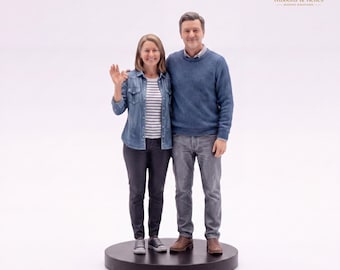 May include: A miniature figurine of two people standing side-by-side on a circular black base. One figure wears a blue denim shirt over a striped top with dark pants, while the other wears a blue knit sweater and gray trousers. The Ribbons & Relics logo is visible in the top right corner.