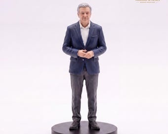 May include: A miniature figurine of an older person with gray hair, wearing a navy blue blazer, a white collared shirt, and dark gray trousers. The figure stands on a circular black base. The text R&R Ribbons & Relics Bespoke Miniatures is visible.