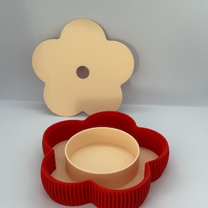 May include: A flower-shaped container set with a red base, a beige interior, and a matching beige lid. The base has a ribbed texture, and the lid has a central hole. The set is designed for storage or display.