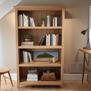 Può includere: Una libreria in legno chiaro con più ripiani pieni di libri, piante e oggetti decorativi. La libreria si trova in una stanza con una scrivania e un piccolo sgabello di legno.