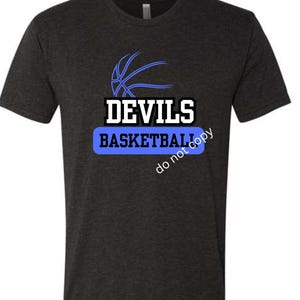 May include: Dark grey t-shirt with a basketball graphic and the words "DEVILS BASKETBALL" in white and blue. The shirt has a crew neck and short sleeves. The design features a basketball and text.