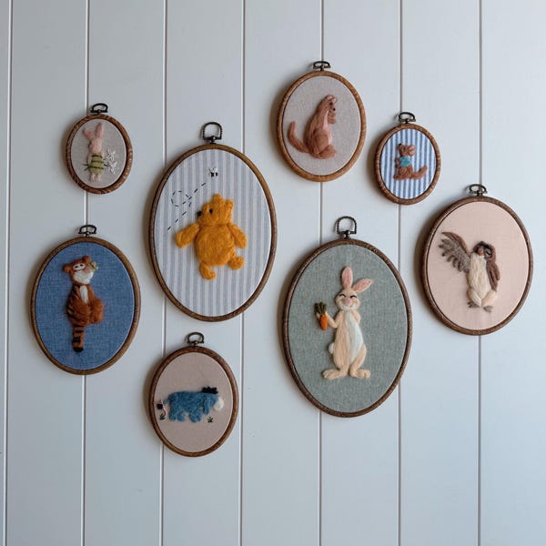 May include: A collection of eight oval wooden embroidery hoops featuring needle-felted characters from the Winnie the Pooh series. The set includes Pooh, Piglet, Tigger, Eeyore, Rabbit, Owl, Kanga, and Roo, each displayed on various fabric backgrounds.
