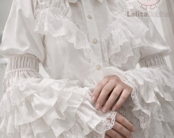 May include: White blouse with ruffled sleeves and a high collar. The blouse features lace trim and decorative buttons down the front. The sleeves are long and gathered at the wrist. The LolitaKokita logo is visible in the upper right corner.