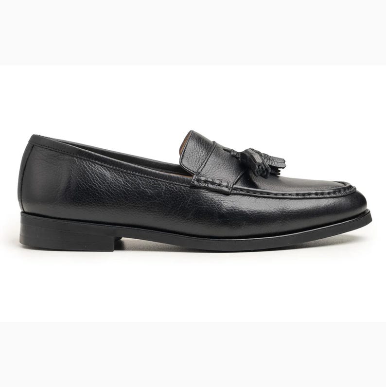 Handmade black full grain leather tassel loafers for men with moc toe stitching, slip-on design, and durable rubber outsole on a white background.