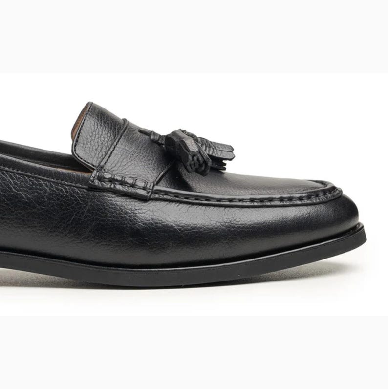 Handmade black full grain leather tassel loafers for men with moc toe stitching, slip-on design, and durable rubber outsole on a white background.
