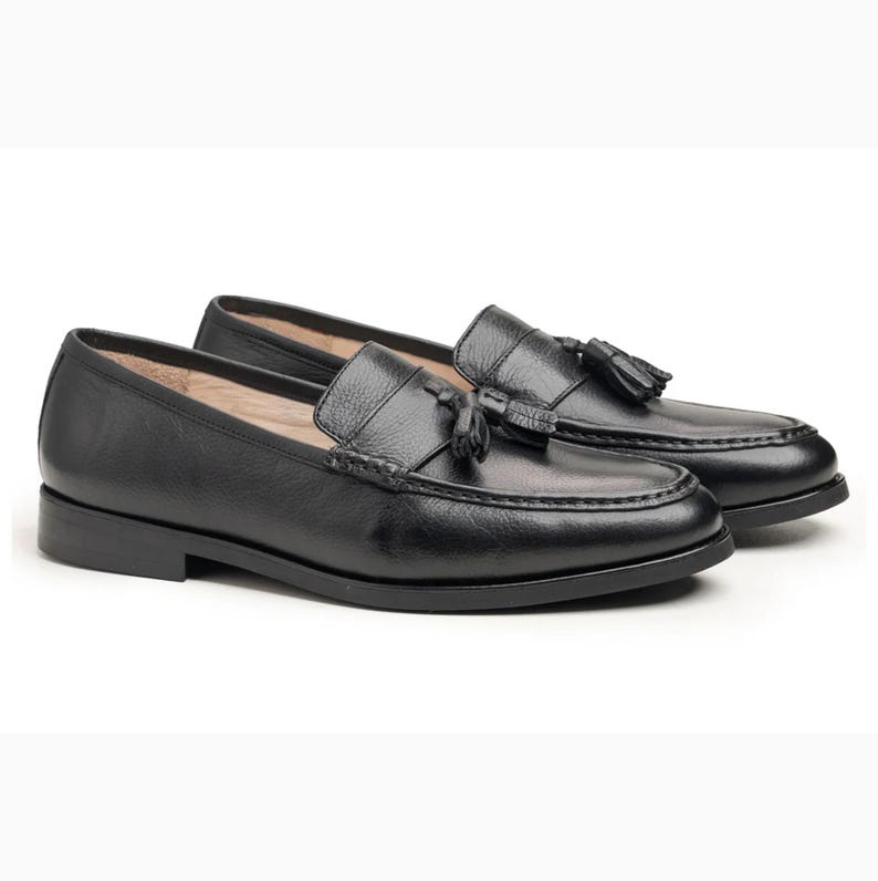 Handmade black full grain leather tassel loafers for men with moc toe stitching, slip-on design, and durable rubber outsole on a white background.