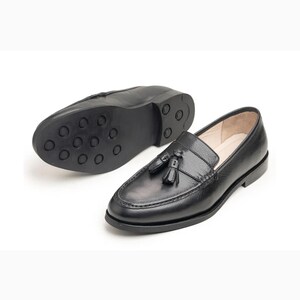 Handmade black full grain leather tassel loafers for men with moc toe stitching, slip-on design, and durable rubber outsole on a white background.
