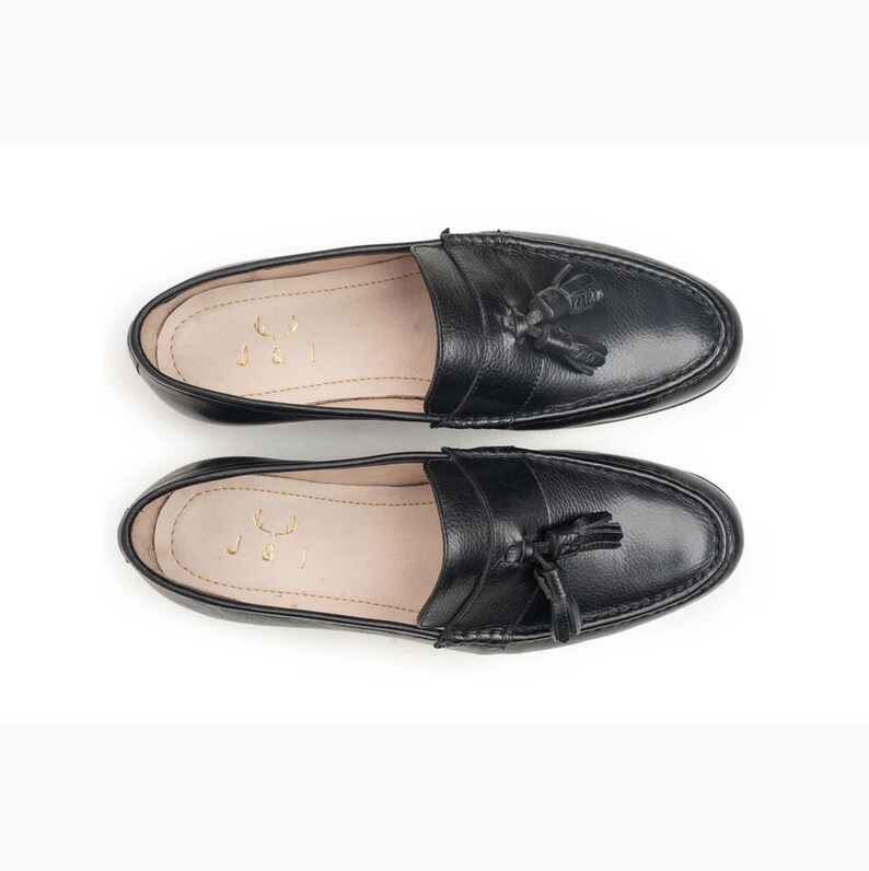 Handmade black full grain leather tassel loafers for men with moc toe stitching, slip-on design, and durable rubber outsole on a white background.