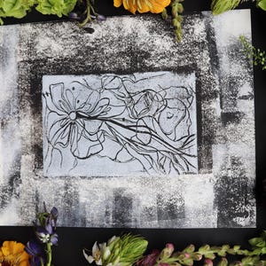May include: Abstract floral art print with black line drawings on a light blue background, framed by a textured black and white border. The artwork is surrounded by colorful flowers, including orange, yellow, and purple blooms.