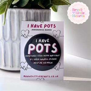 May include: A black awareness badge with the text "I HAVE POTS" in white and pink. The badge also includes the text "SOMETIMES I FEEL DIZZY AND FAINT IF I SEEM UNWELL, PLEASE HELP ME LIE DOWN." The badge is on a white card.