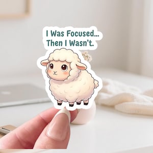 Puede incluir: Una pegatina con un cordero de dibujos animados y el texto "I Was Focused... Then I Wasn't." El cordero tiene un pelaje blanco y esponjoso, ojos marrones y pezuñas negras. Ideal para decorar cuadernos, ordenadores portátiles u objetos personales.
