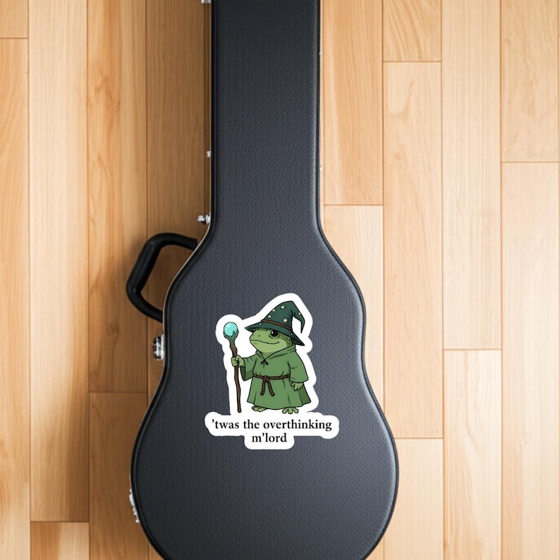 May include: A sticker depicting a cartoon frog in a wizard's outfit, including a green robe and a hat with white spots, holding a staff with a blue orb. The text says, "'twas the overthinking m'lord."