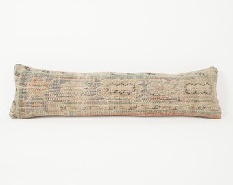 May include: A long, rectangular pillow with a faded, patterned design. The pillow features a mix of colors, including beige, blue, and orange, creating a vintage aesthetic. The pillow is a decorative item, likely for a bed or sofa.