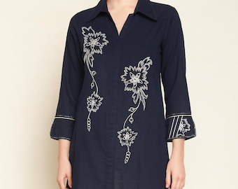 May include: Navy blue tunic-style shirt with white floral embroidery. The long-sleeved shirt features a V-neck collar and decorative embroidery down the front and on the cuffs. The shirt is paired with white pants.
