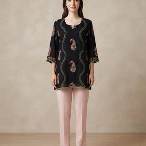 May include: A black tunic featuring three-quarter length sleeves, a scoop neckline with a small notch, and a scalloped hem. The garment is decorated with vertical wavy lines of green embroidery and floral paisley motifs in red and gold tones.