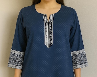 May include: A navy blue tunic with a subtle polka dot pattern. The tunic features a decorative white and black embroidered design along the neckline and sleeve cuffs. The sleeves are three-quarter length.