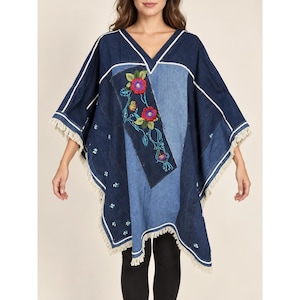 May include: A V-neck denim poncho featuring a patchwork design of dark and medium blue fabric panels. The garment is decorated with vibrant red and purple floral embroidery, white piping accents along the seams, and a frayed fringe hemline.