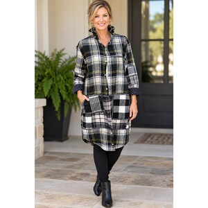 May include: A long-sleeved button-down shirt featuring a black, white, and yellow plaid pattern. The garment includes a collar, two large front pockets with a contrasting plaid design, and dark cuffs with a white polka dot pattern.