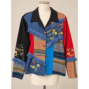 May include: A long-sleeve button-down jacket featuring a patchwork design of black, red, blue, and denim fabric panels. The jacket includes decorative fringe trim, embroidered yellow flower motifs, and horizontal patterned bands across the front and sleeves.