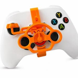 May include: White gaming controller with an orange steering wheel attachment. The controller features black, green, and yellow buttons. The steering wheel attachment has a gear-like design and is secured with an orange strap.