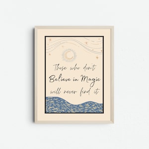 Könnte beinhalten: Gerahmter Kunstdruck mit dem Zitat "Those who don't Believe in Magic will never find it." Das Kunstwerk zeigt einen beigen Hintergrund mit einem Halbmond, Sternen und einem blauen Wellenmuster. Der Rahmen ist hellbeige.