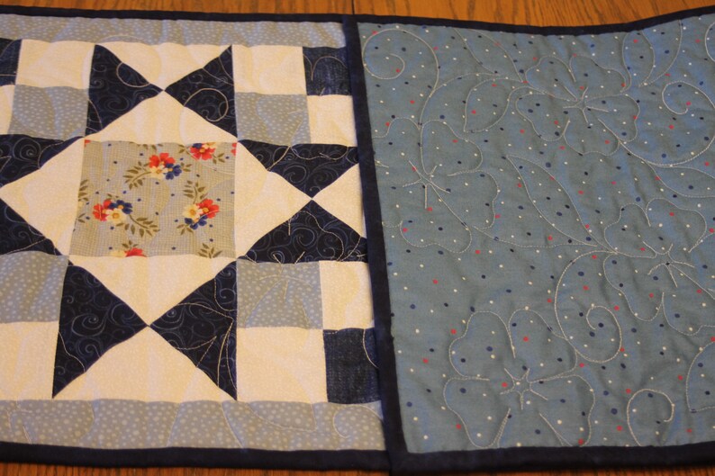 Puede incluir: Un camino de mesa acolchado azul y blanco con un patr&oacute;n floral en el centro y un patr&oacute;n de lunares azul y blanco en los lados.