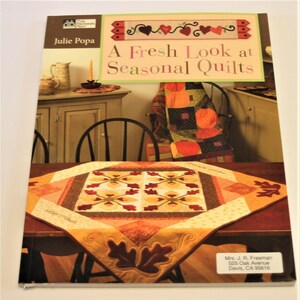 Op de afbeelding: Boekomslag met een quilt met een herfstbladerenontwerp. De titel van het boek is "A Fresh Look at Seasonal Quilts" van Julie Popa. De boekomslag bevat ook een foto van een quilt in rood, oranje en gele kleuren.