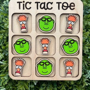 May include: A wooden tic-tac-toe game with green and orange cartoon characters. The game board has the words "Tic Tac Toe" printed on it.