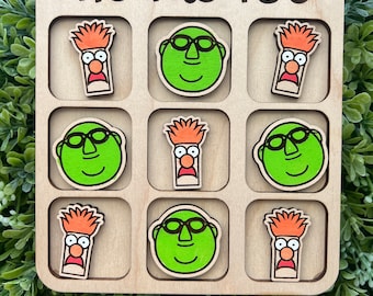 May include: A wooden tic-tac-toe game with green and orange cartoon characters. The game board has the words "Tic Tac Toe" printed on it.