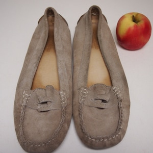 May include: A pair of light brown suede loafers with a decorative stitch detail around the toe and a small strap across the top.