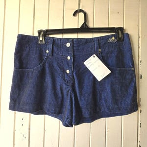 May include: Blue corduroy shorts with a button fly and side pockets. The shorts have a white tag with the text "Women's Corduroy Shorts Size 30" written on it.