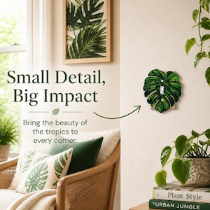 May include: A green, leaf-shaped light switch cover is mounted on a cream-colored wall. The switch cover is a detailed replica of a monstera leaf. The image also shows a framed botanical print, throw pillows, and potted plants, with the text "Small Detail, Big Impact."