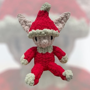 May include: A handmade crochet elf doll in a festive red outfit with a matching hat. The elf has light gray ears, a light gray face, and light green accents on the hat, collar, hands, and feet. The doll is a whimsical holiday decoration.