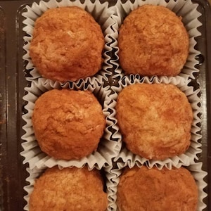 May include: Six round, brown, chocolate-covered treats in individual white paper cups. The treats are arranged in two rows of three, in a brown box.