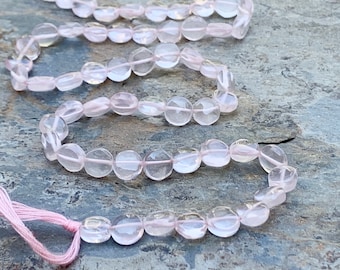 May include: A strand of pale pink rose quartz beads, each bead is faceted and has a slightly rounded shape. The beads are strung on a thin pink thread.