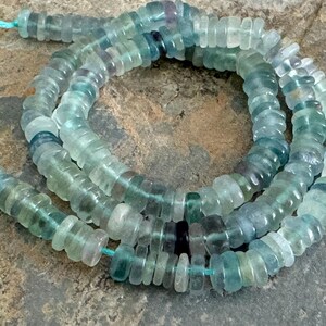 Könnte beinhalten: Eine Strähne aus hellblauen und grünen Edelsteinperlen. Die Perlen sind facettiert und haben eine leicht unregelmäßige Form. Die Perlen sind auf einem durchsichtigen Faden aufgefädelt.
