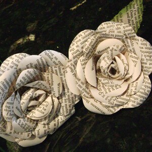 May include: Two paper roses made from the pages of a book. The roses are white and have a delicate, layered appearance. The text on the pages is visible and includes words like "Wuthering Heights" and "Heights".