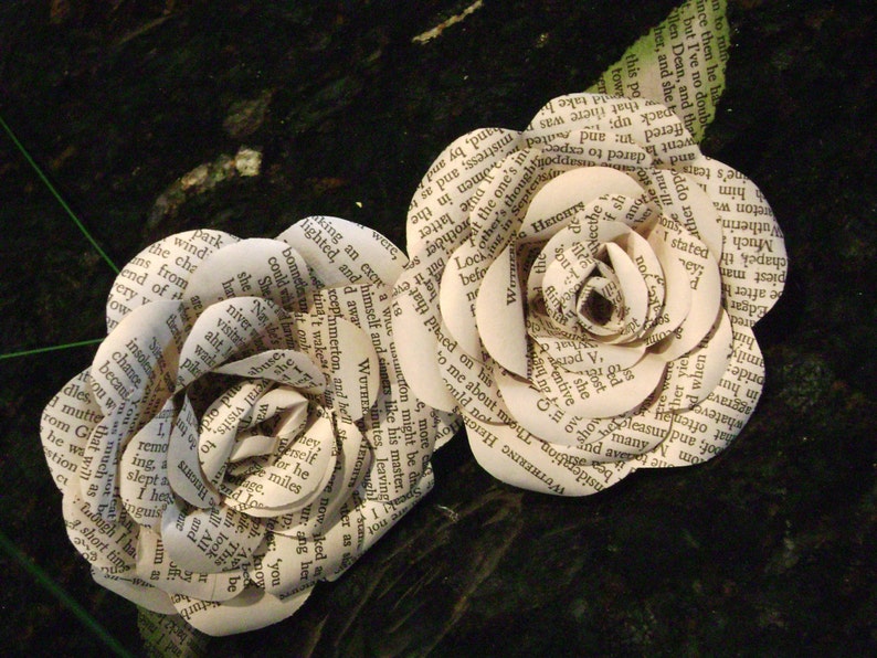 May include: Two paper roses made from the pages of a book. The roses are white and have a delicate, layered appearance. The text on the pages is visible and includes words like "Wuthering Heights" and "Heights".