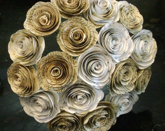Peut inclure: Un bouquet de roses en papier fabriquées à partir de vieilles pages de livres. Les roses sont disposées en cercle et sont de tailles différentes. Les roses sont de couleur crème et ont un aspect vintage.