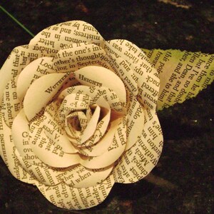 May include: A paper rose made from the pages of a book. The rose is a light cream color and has a delicate, layered design. The text on the pages is visible, including the title "Wuthering Heights".