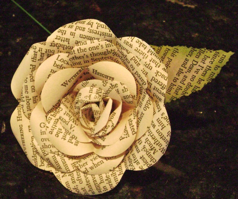 May include: A paper rose made from the pages of a book. The rose is a light cream color and has a delicate, layered design. The text on the pages is visible, including the title "Wuthering Heights".