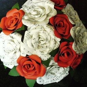 May include: A bouquet of red and white paper roses made from sheet music. The roses are arranged in a circular pattern and have a vintage aesthetic.
