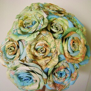 May include: A bouquet of paper roses made from maps in shades of blue, green, and yellow. The roses are arranged in a circular shape and are tied together with a ribbon.
