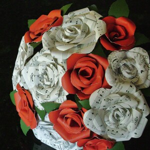 May include: A bouquet of red roses with white paper roses, each with musical notes printed on them. The bouquet is tied with green ribbon and leaves.