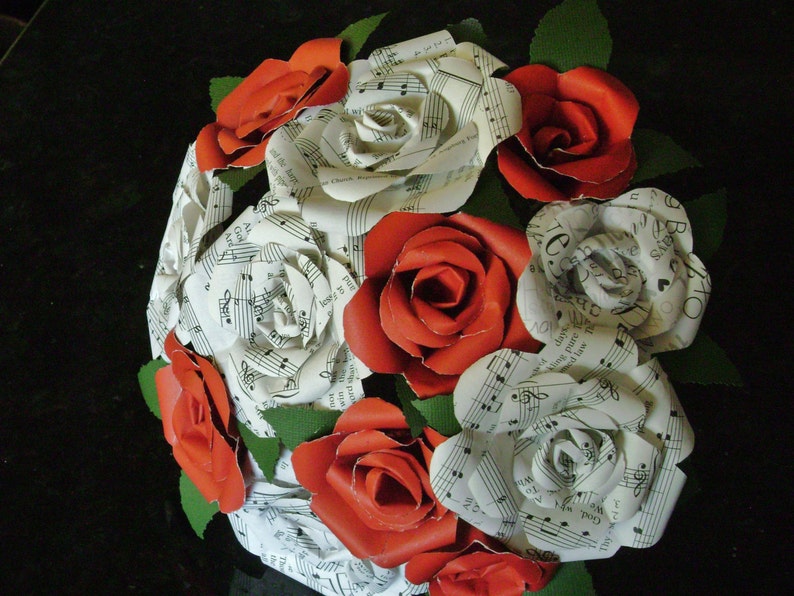 May include: A bouquet of red roses with white paper roses, each with musical notes printed on them. The bouquet is tied with green ribbon and leaves.